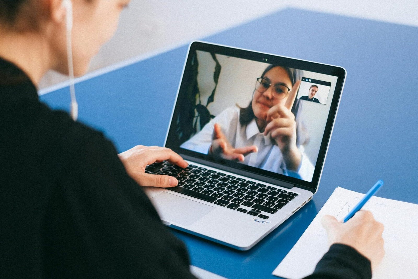 Woman participating in a virtual meeting, taking notes during a video conference on a laptop.